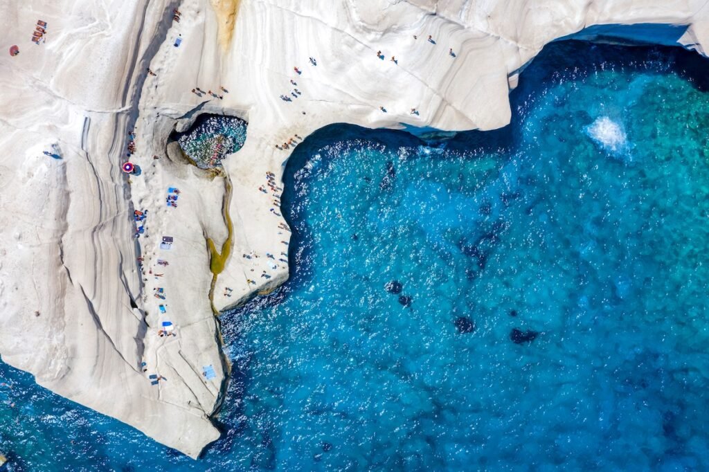 Aerial view to the chalk rock formations of Sarakiniko with people enjoying the sparkling blue sea on a hot summer day, Milos island, Cyclades, Greece, Charming & Timeless: Best European Destinations for Your Next Great Escape
