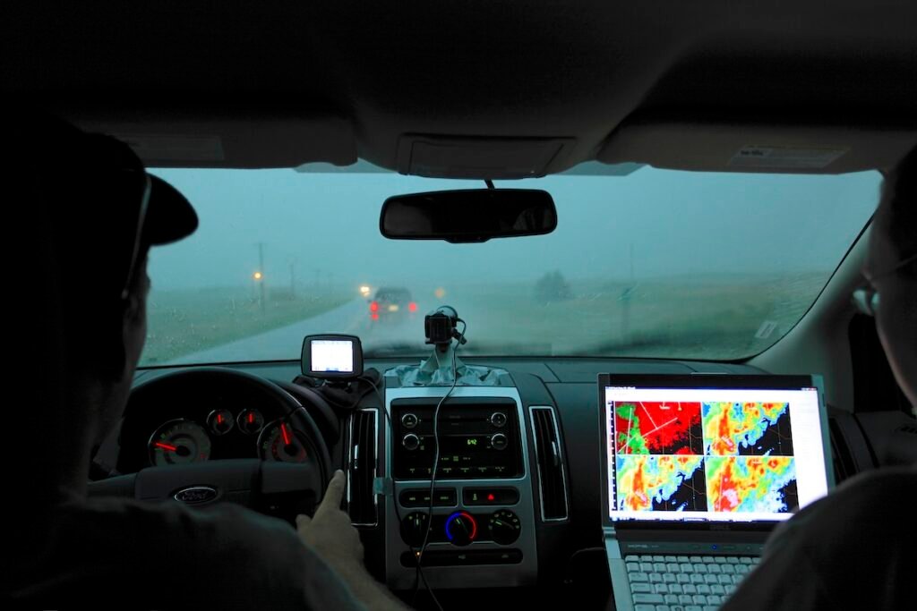 Valentine (NE), USA - Two storm chasers drive north along Highway 97 in pursuit of a severe weather event in Nebraska. They are driving through heavy rain while monitoring various radar data sources on a laptop computer to locate the centre of the storm. A video camera mounted on the dashboard is used to record the storm and a GPS navigation device assists highway and road selection.