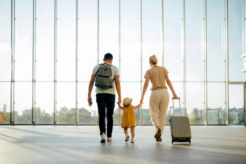 Back view of husband and his wife walking with their little girl and suitcase at the airport 