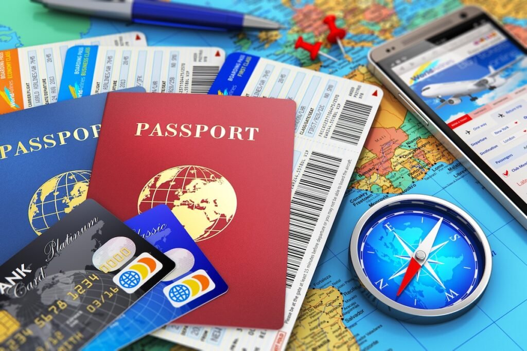 Creative abstract business travel and tourism concept: air tickets or boarding pass, passports, touchscreen smartphone with online airline tickets booking or reservation internet application, magnetic compass, credit cards and pen on world geographic map atlas with selective focus effect 