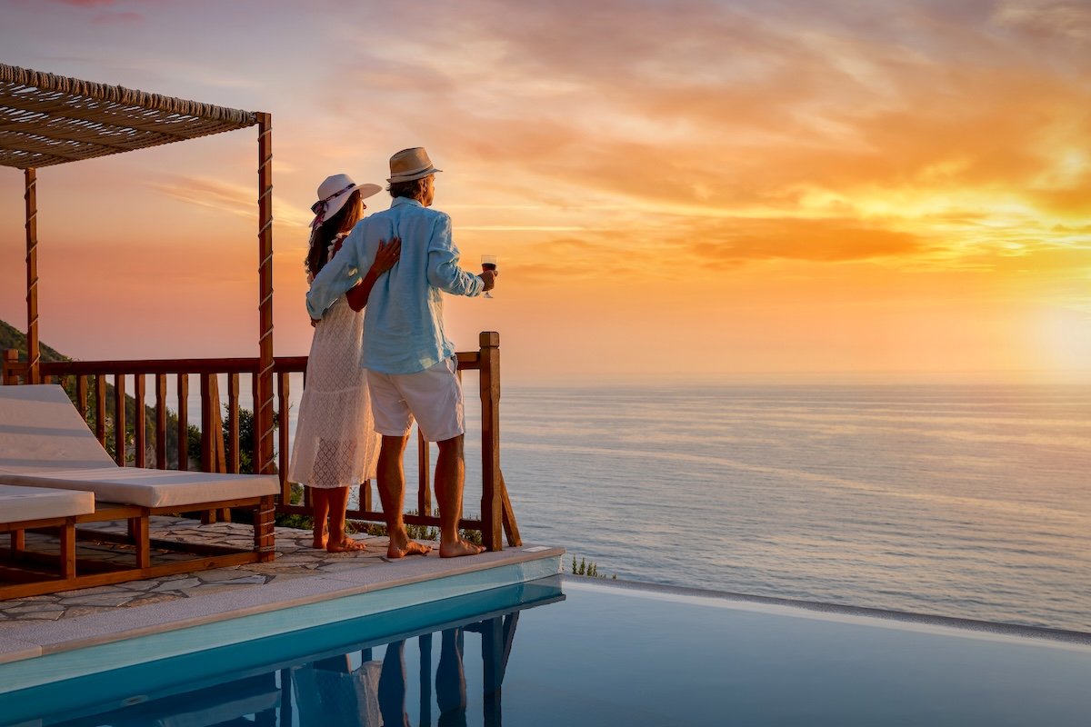 A romantic couple on summer vacation enjos the sunset over the mediterranean sea by the pool with a glass of Aperitif tropical getaway