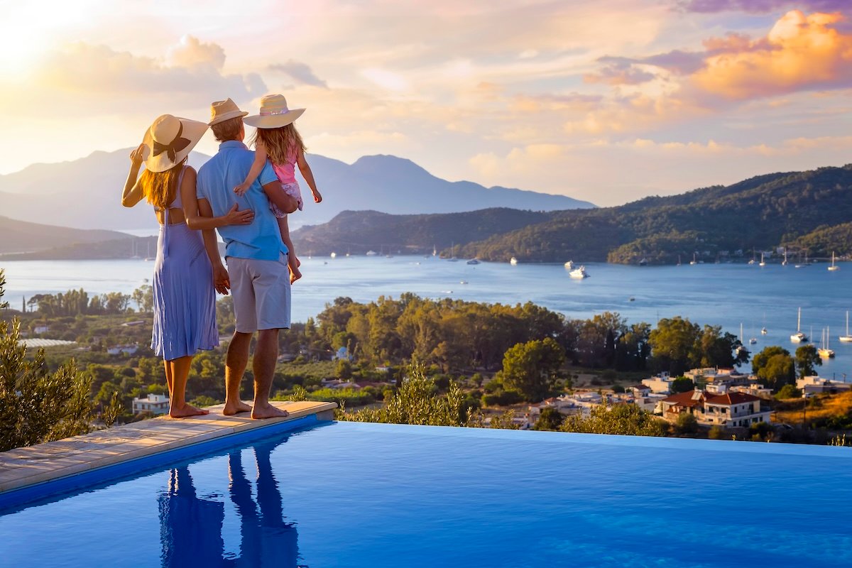 What Are the Most Affordable Family Vacation Ideas for 2025 Travelers? # Part 1 A family on summer holidays stands by the swimming pool and enjoys the beautiful sunset behind the mountains and the sea