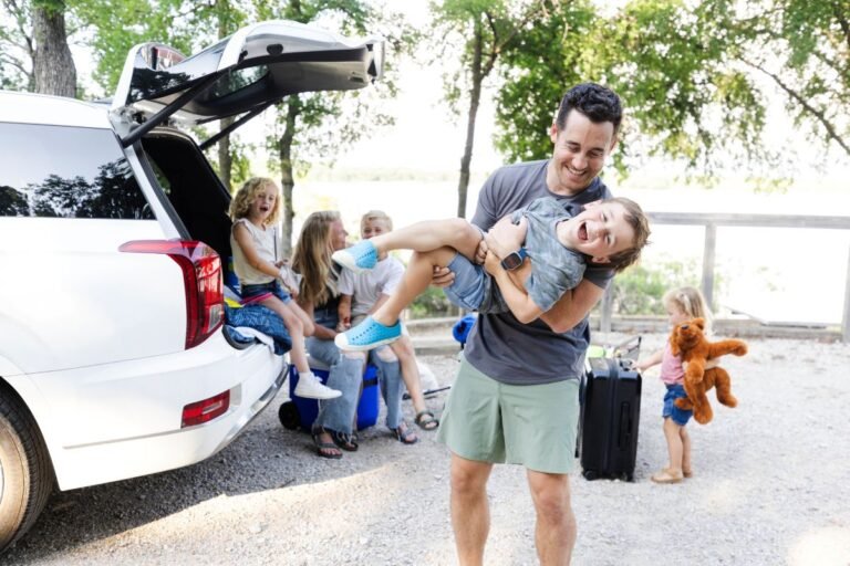 Happy family loading car for a budget road trip vacation &mdash; budget family travel tips