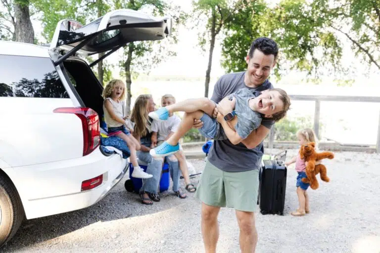 Happy family loading car for a budget road trip vacation — budget family travel tips