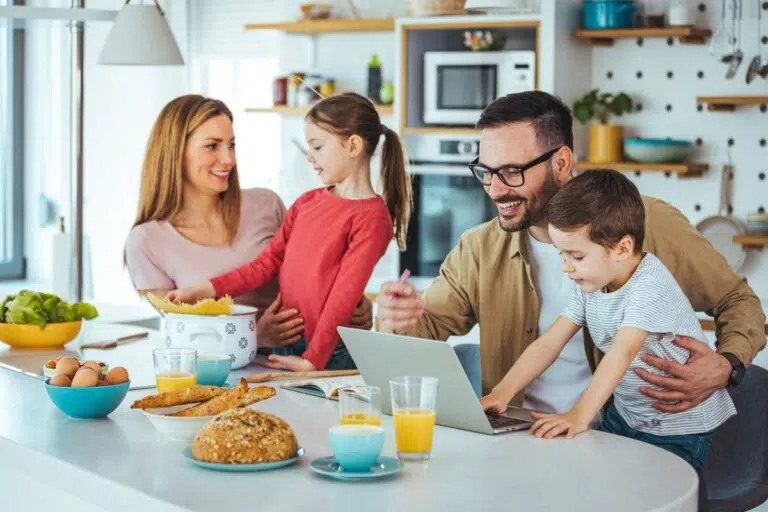 Family gathered around laptop at kitchen counter planning a vacation &mdash; best time to book Travelocity family packages