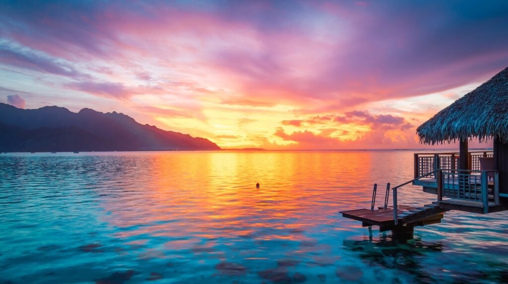 Stunning lagoon landscape with overwater bungalow against colorful clouds sky during sunset in Moorea, French Polynesia.