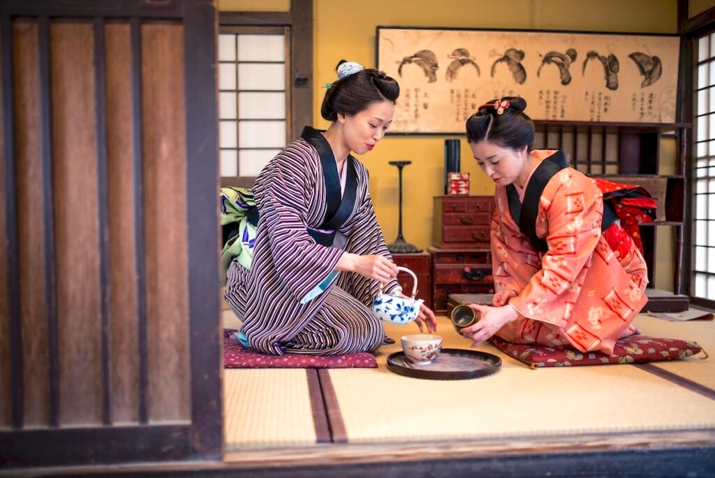 Two Japanese women wearing a kimono drinking tea indoors, in tea room. They are talking and having fun. coolest vacation spots