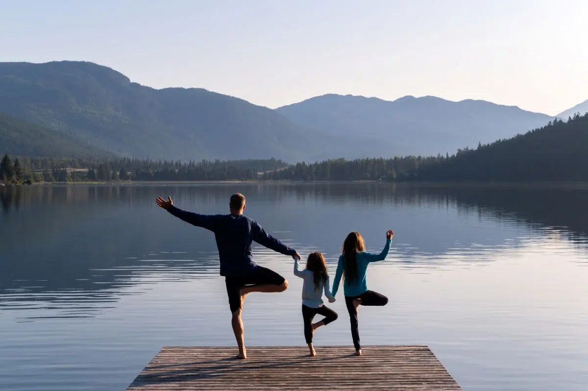 Family doing tree pose yoga together on a dock by a mountain lake, one of the best budget family wellness retreats under $200 per person