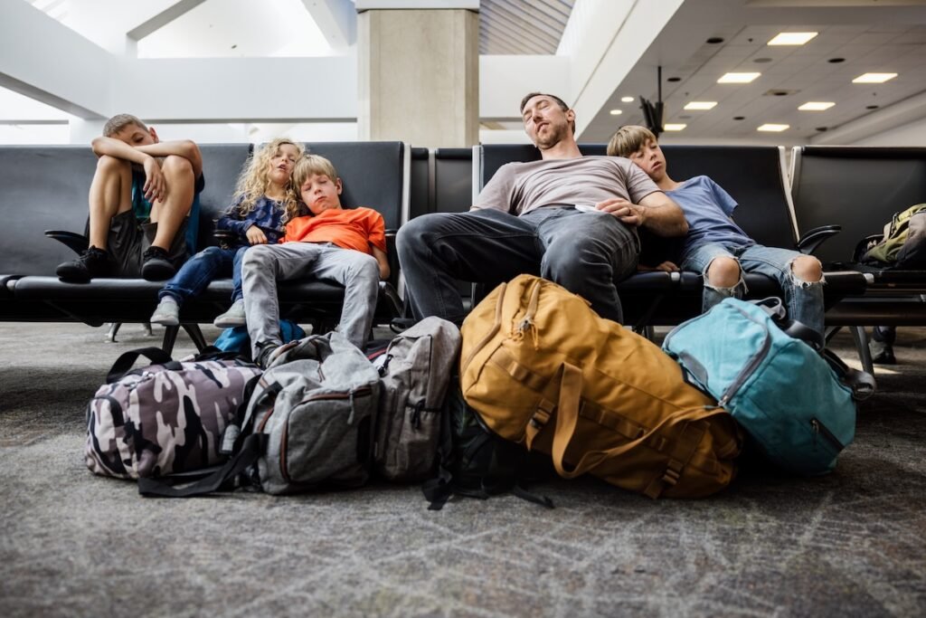 Exhausted dad and three tired kids surrounded by bags at airport — family vacation mistakes to avoid