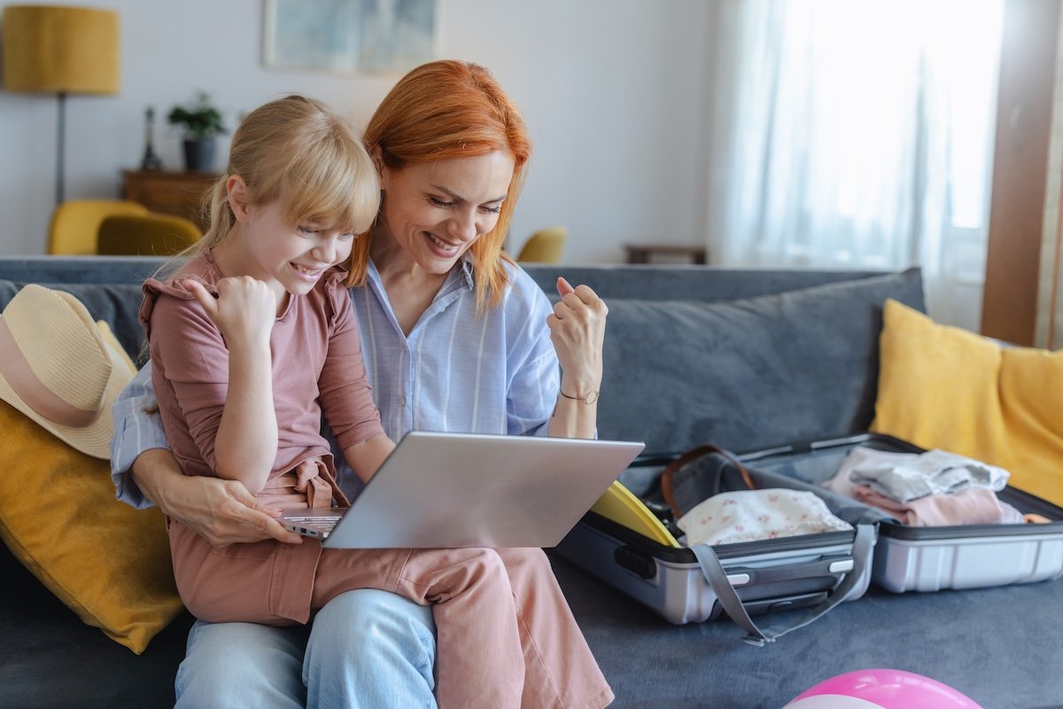 Mom and daughter celebrating finding a cheap flight deal on laptop at home &mdash; Travel Tuesday flight deals for families
